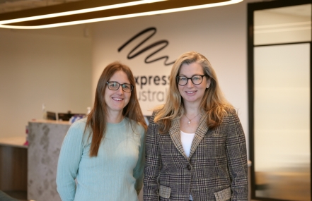 Bianca and Rebecca smiling to camera in front of a reception desk to Expression Australia