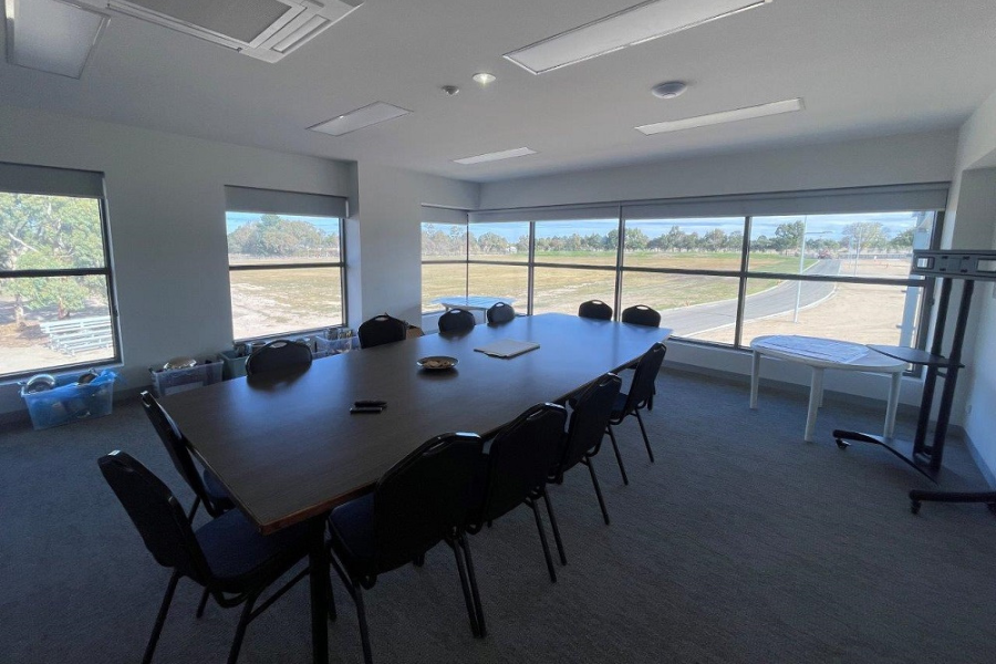 Large table with 12 chairs in meeting room. Windows behind looking out.