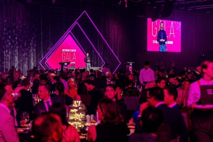 Red-tinged lighted formal event with many guests at tables.