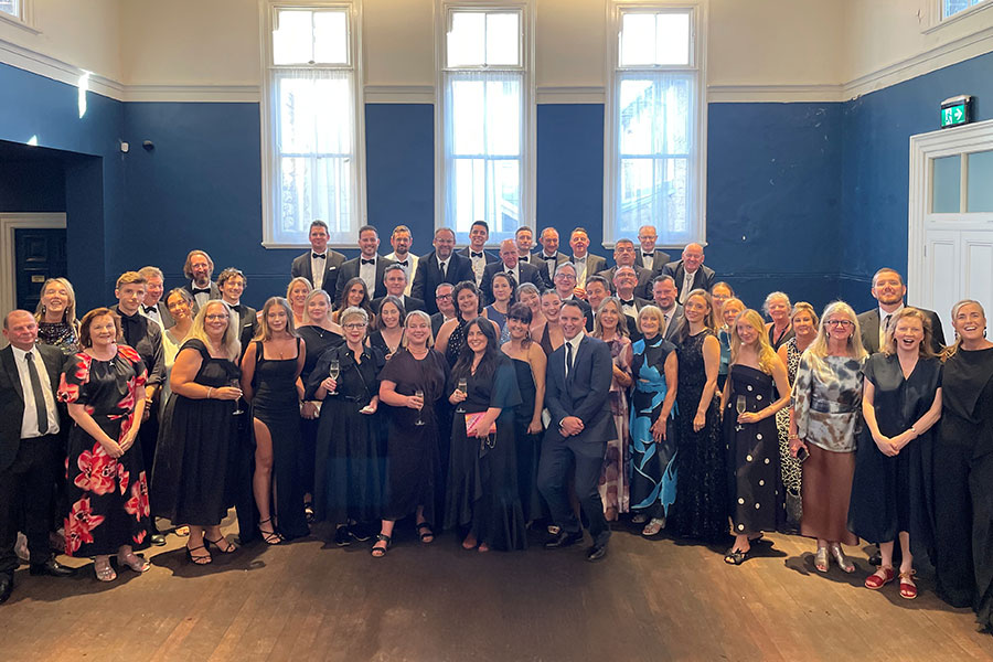 A large group of people dressed in formal attire pose for a photograph in an elegant room with blue walls and tall windows for the Australian Tourism Awards.