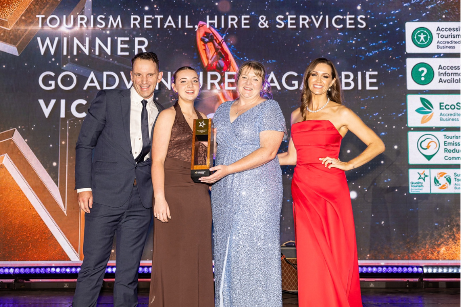 Go Adventure Nagambie winners of Tourism Retail Hire and Services Four people posing together at an awards event. One person is holding a trophy. The backdrop displays the text: "Tourism Retail, Hire & Services Winner, Go Adventure Nagambie, Victoria." Several icons and logos are visible on the right side of the backdrop.
