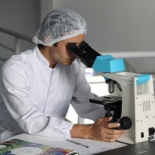 Person in lab coat looking into microscope
