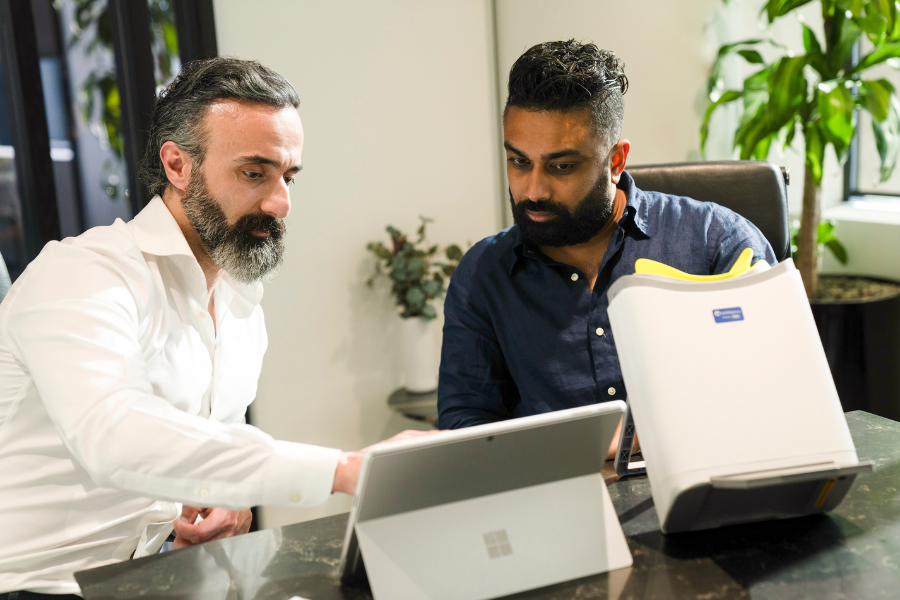Two medical research professionals working together at a table with a laptop and retinal scanner.