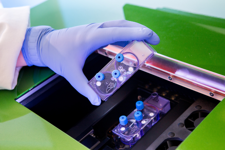A scientist's gloved hand placing a multi-well plate into a laboratory machine.