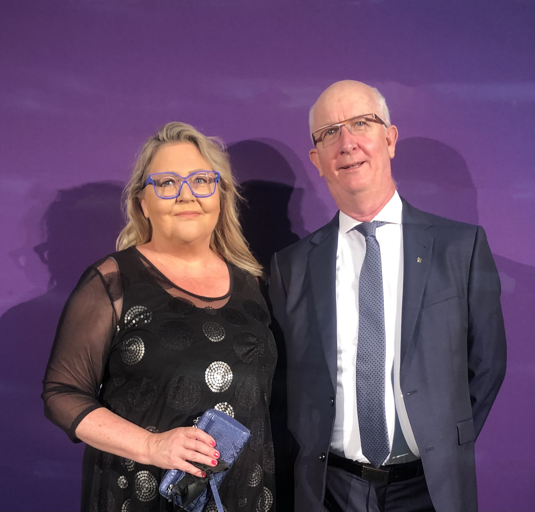 A close up of a couple smiling with a purple wall behind them