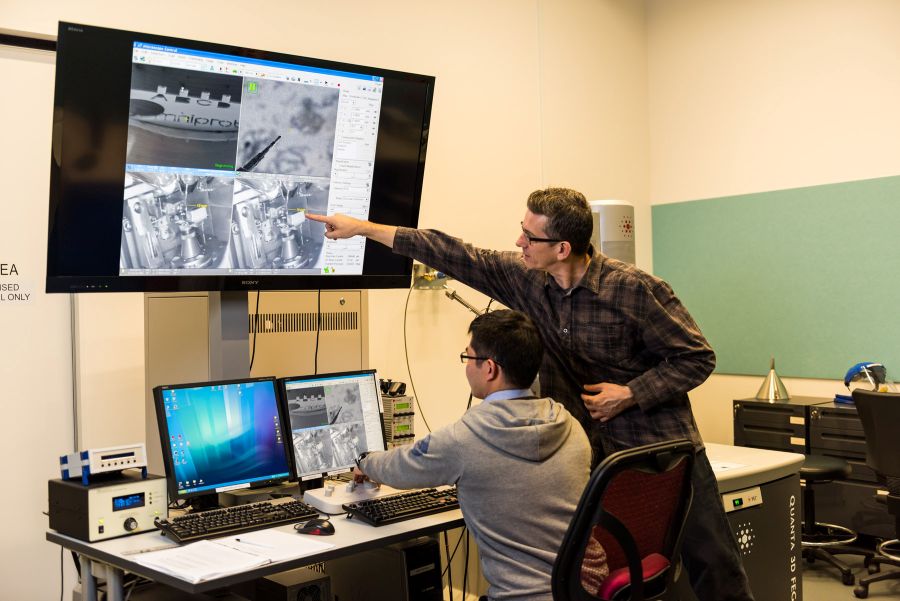 Two individuals working at a computer setup. One is pointing at the screen