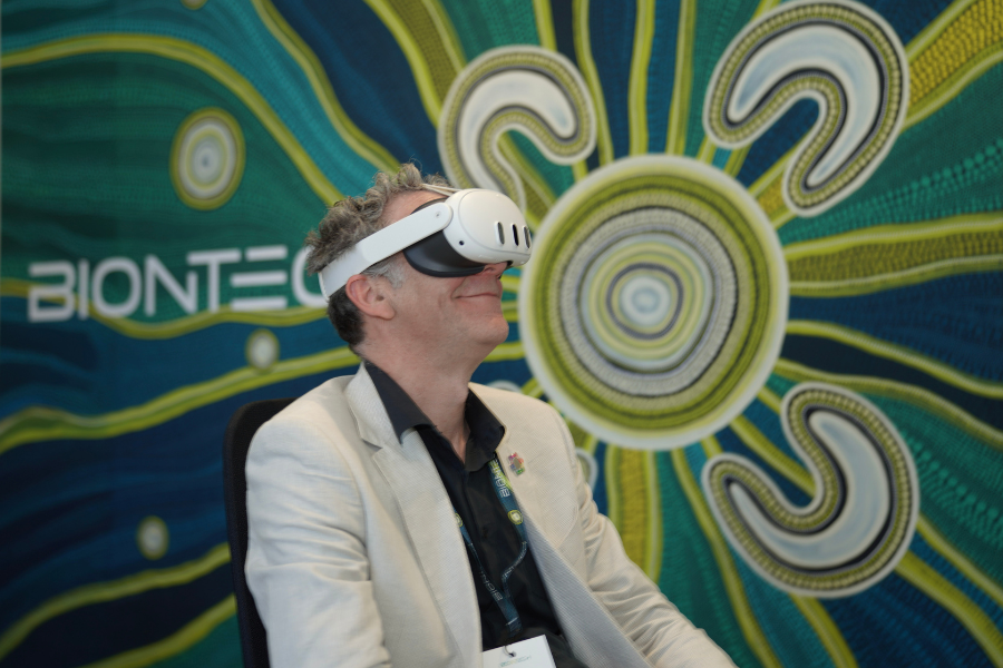 A person is seated wearing a virtual reality headset in front of a colourful, abstract artwork featuring swirling patterns. The word 