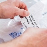 Two hands placing a label on a clear bag that reads 'these calf sleeves didn't go to landfill'.