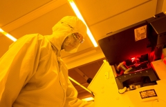 Under orange lights, a person in full medical PPE looks into a microscope