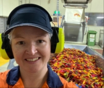 Photo of worker at the Nestle factory with a conveyor belt of snake lollies in the background.