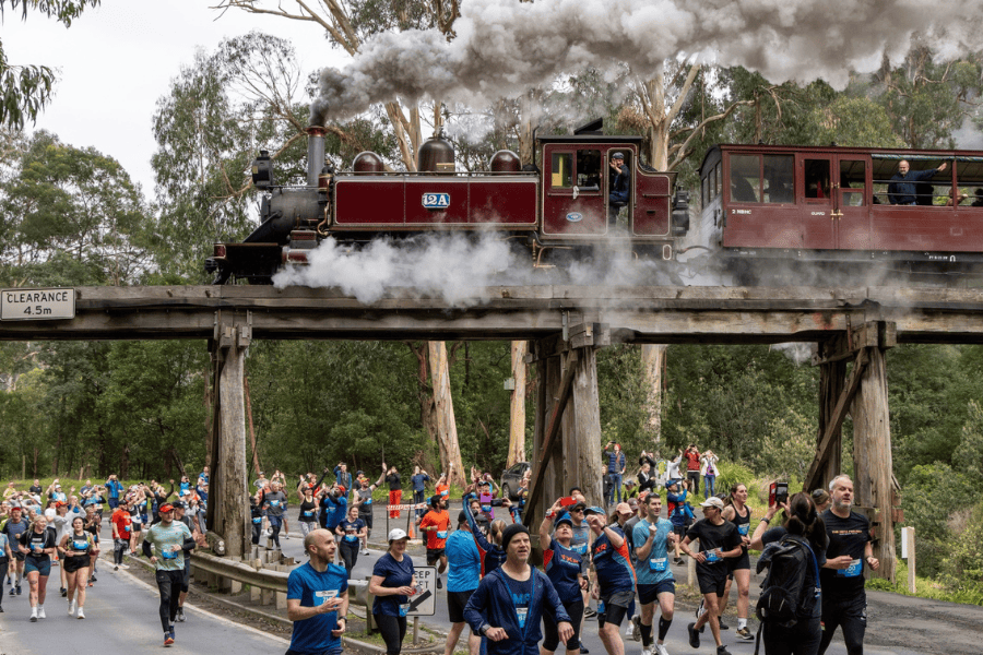 Huge crowd of first wave of runners at the start of a race. Steam train above on track bridge going over the road with the runners