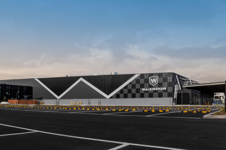 Exterior view of the Walkinshaw facility with a large logo on the building, featuring a modern geometric design and a clear blue sky in the background.