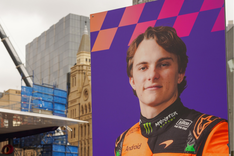 Formula 1 themed banner with picture of Oscar Piastri at Federation Square with Melbourne CBD buildings 