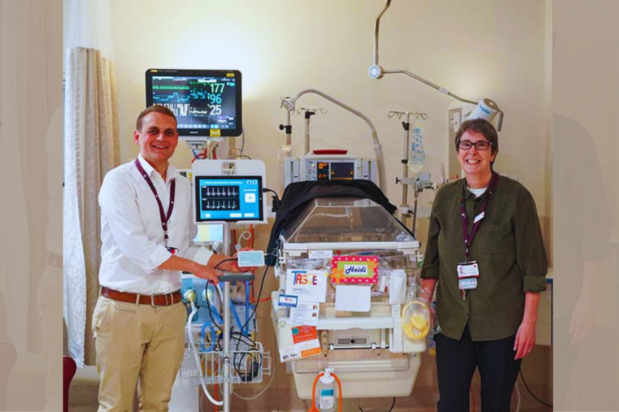 Two people stand in a hospital holding a medical device at a neonatal intensive care unit.