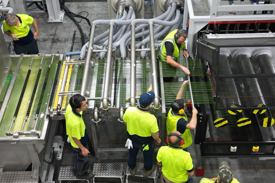 Aerial view of workers in high-visibility clothing operating machinery at a production facility. 