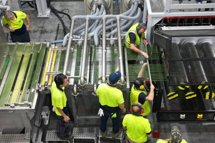 Aerial view of workers in high-visibility clothing operating machinery at a production facility. 