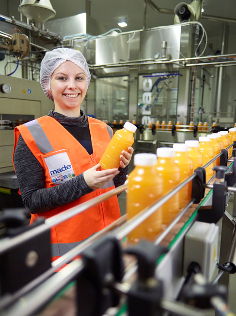 Worker inspects a bottle of orange juice from a food manufacturing production line
