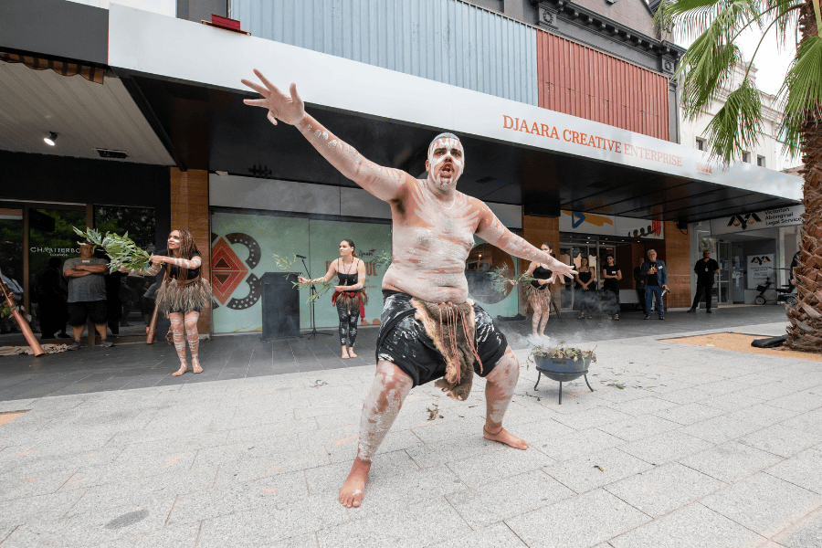 An indigenous person performing in front of Djarra Creative Enterprise building in traditional dress