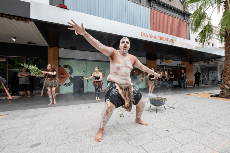 An indigenous person performing in front of Djarra Creative Enterprise building in traditional dress