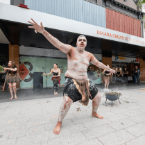 An indigenous person performing in front of Djarra Creative Enterprise building in traditional dress