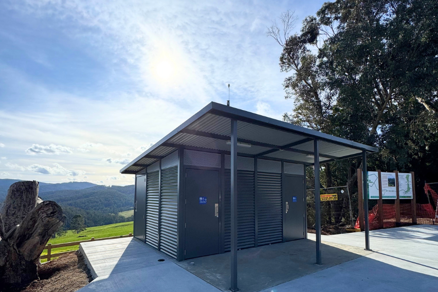 A newly built public toilet located in a scenic area with expansive views of a valley. Sunlight shines from the left, and informational signs are visible.