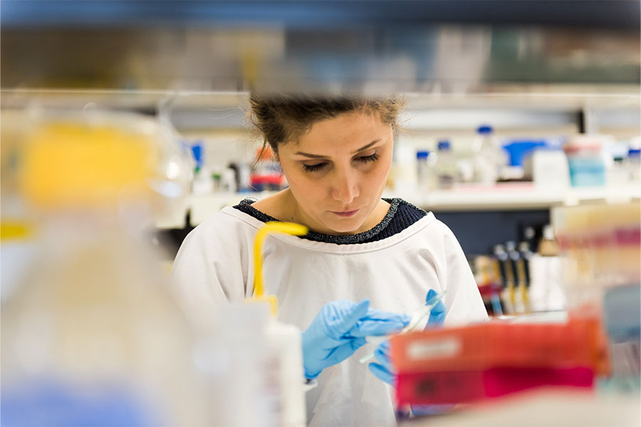 A worker in personal protective equipment prepares a microscope slide in a lab.