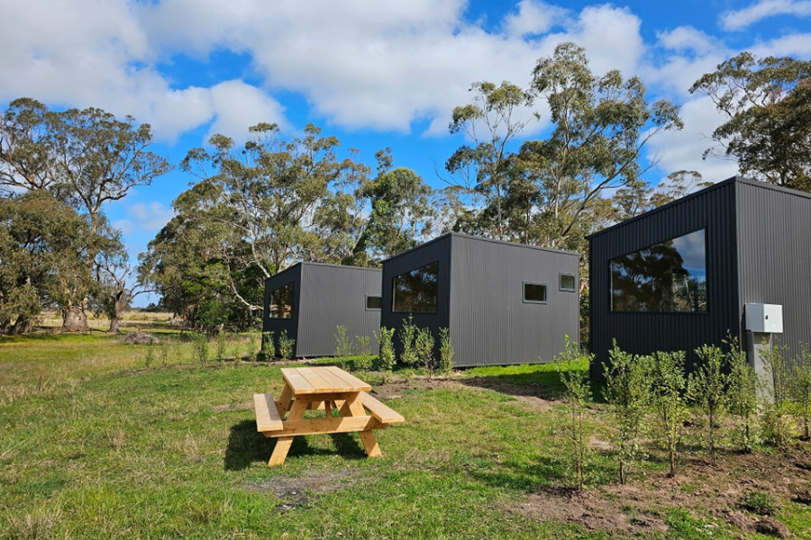 3 small housing pods positioned in nature with a picnic table in foreground