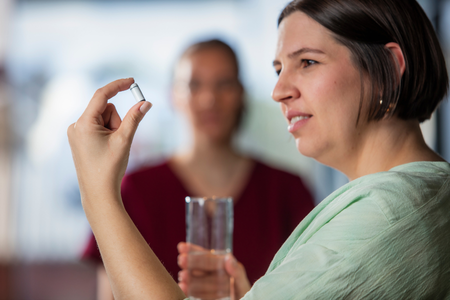 Person is holding up a white capsule with black ends looking at it with curiosity with 