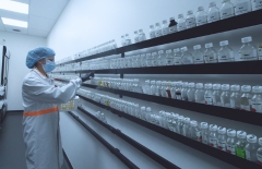 A person in protective gear including hairnet and mask is looking at rows of jars on a wall