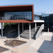 Exterior view of the learning hub with a prominent red overhanging structure, wide staircases, and surrounding outdoor seating areas.