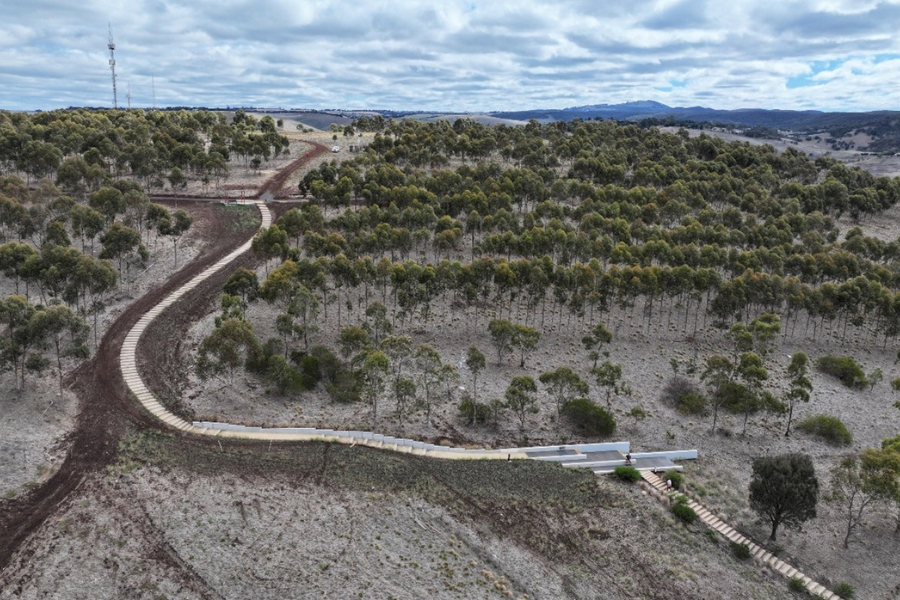 A new path with steps weaving down a hill with a low amount of vegetation. 