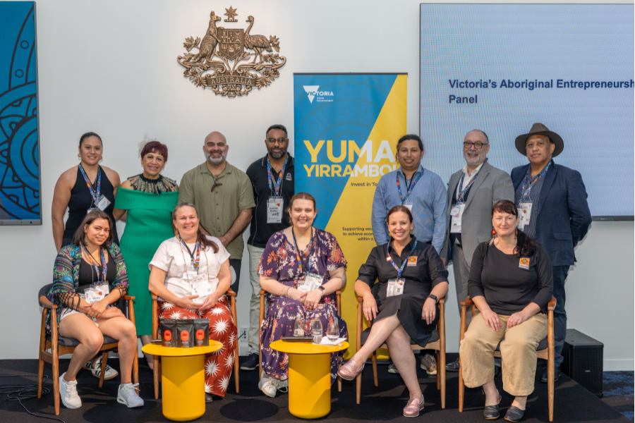 Group of 10 individuals posing representing the Victoria's Aboriginal Entrepreneurs Panel, with a backdrop featuring a Yuma Yirramboi banner, Victorian Government logo and Australian Government emblem.