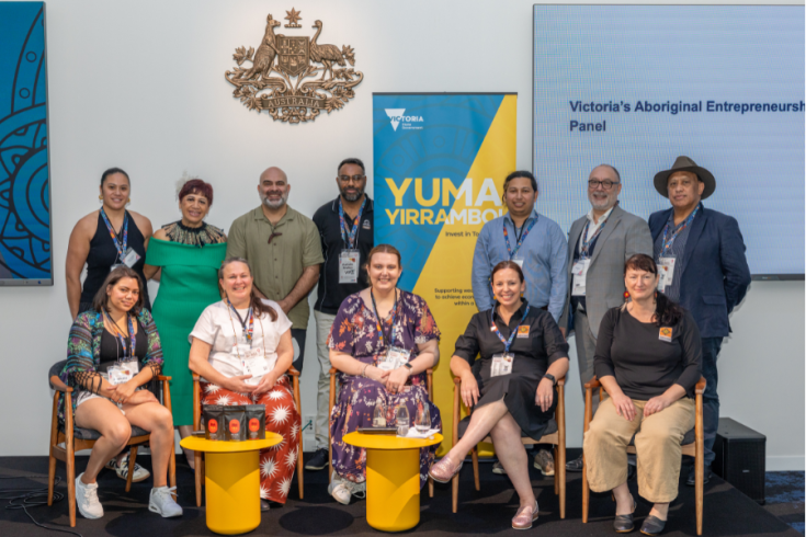 Group of 10 individuals posing representing the Victoria's Aboriginal Entrepreneurs Panel, with a backdrop featuring a Yuma Yirramboi banner, Victorian Government logo and Australian Government emblem.