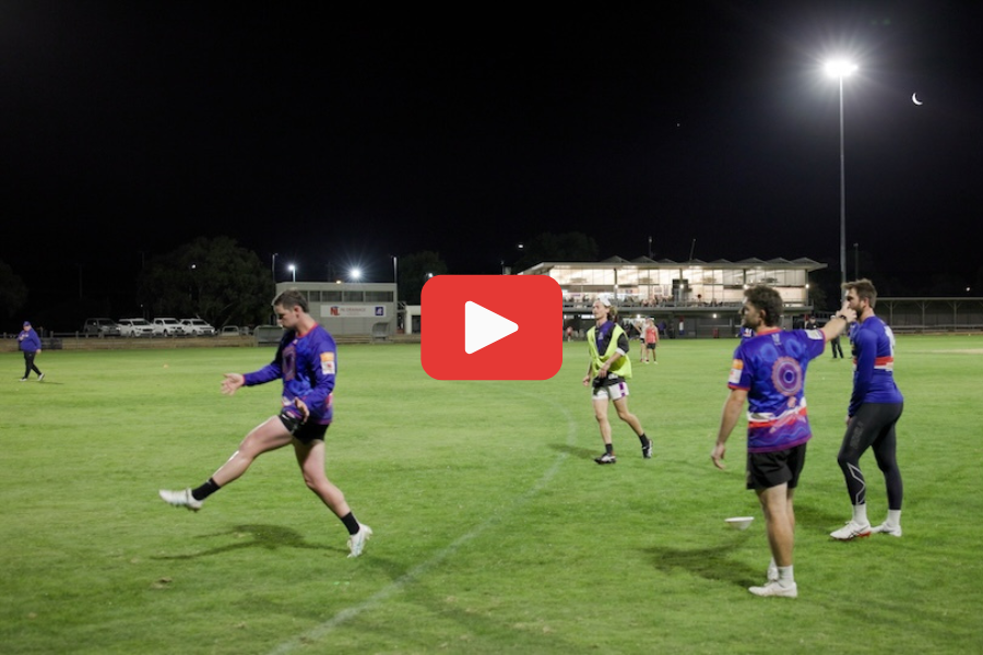 Tatura Football Club players doing a kicking line drill on the oval of Tatura Park underneath a large light tower