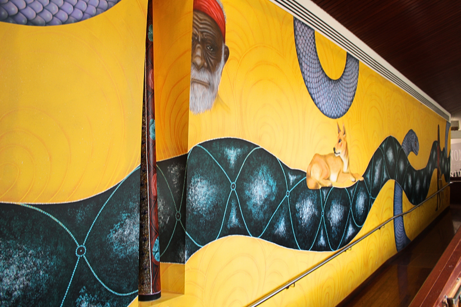 A portion of the mural created by Yorta Yorta artist Stuart Hearn. Featuring a yellow background with serpant weaving throughout figures and animals. 
