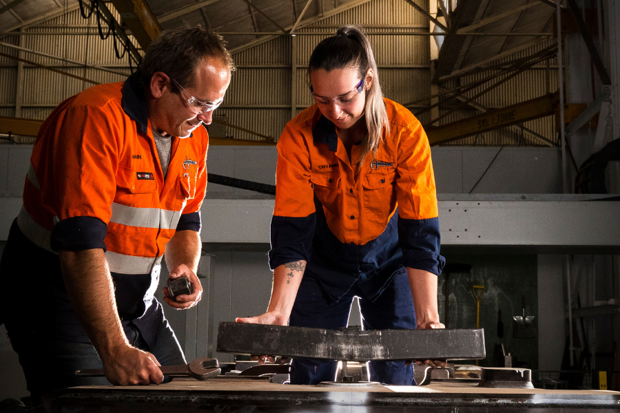 Two people in high vis clothing are bending over a piece of machinery