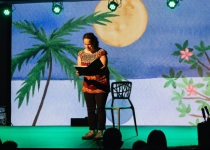 A female on stage reading with a colourful background