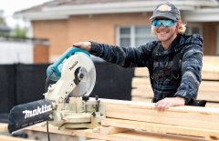 Jack Kelsey wears reflective wrap around sunglasses and a baseball hat, holding a Makita tool over some wood