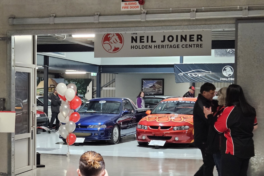 New showroom with doors open and two cars on display. There is a sign that reads  ‘The Neil Joiner Holden Heritage Centre’ above the doorway. 