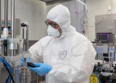 Technician in PPE, mask and gloves filling vials