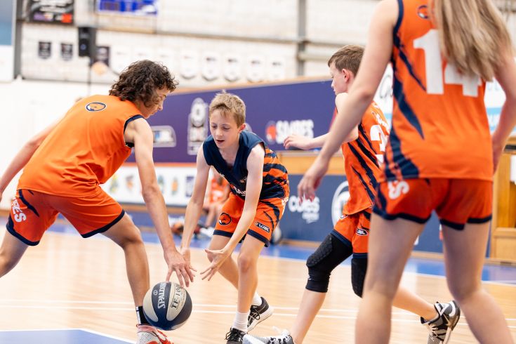 Kids playing basketball in an indoor stadium.