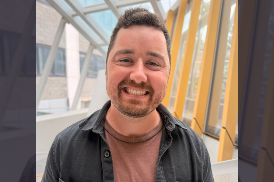 Jessy has dark hair and a beard and is smiling in a bright room.