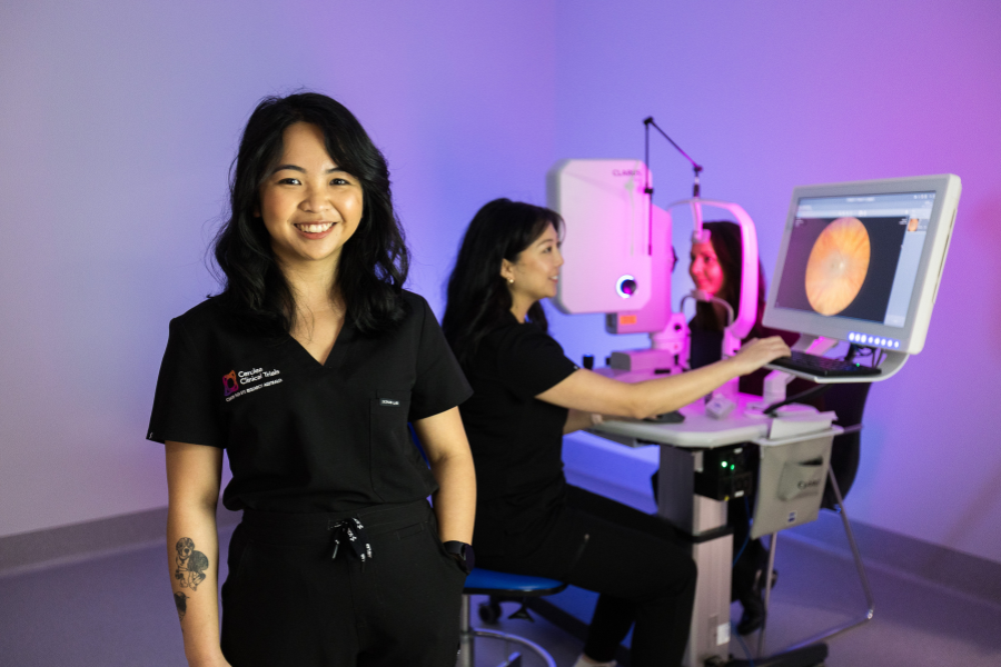 A medical professional in a lab coat smiling at the camera, and another professional working with medical equipment in the background