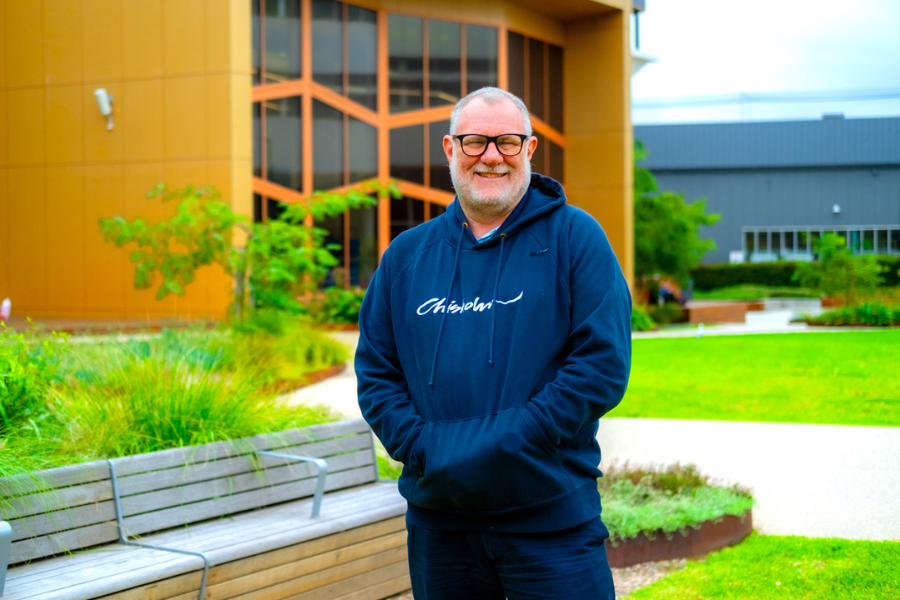 Chris standing in front of a TAFE building entrance with his hands in his pockets.