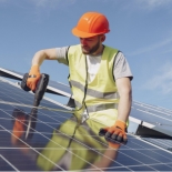 Worker in high vis vest and orange hard hard installing solar panels outside on a sunny day