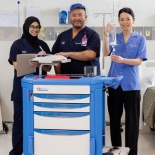 Three people standing in a medical setting with medical equipment