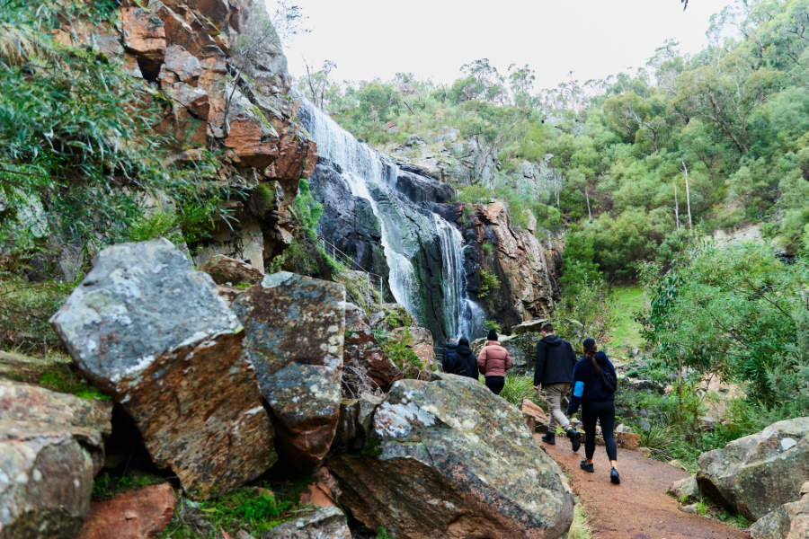 Three people walking on a trail past rock with a waterfall in the background