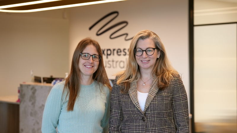 Bianca and Rebecca smiling to camera in front of a reception desk to Expression Australia