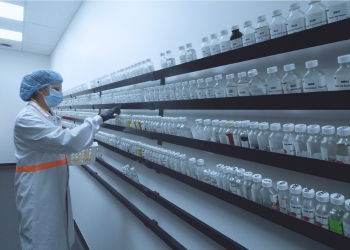 A person in protective gear including hairnet and mask is looking at rows of jars on a wall at the Essential Flavours and Ingredients laboratory