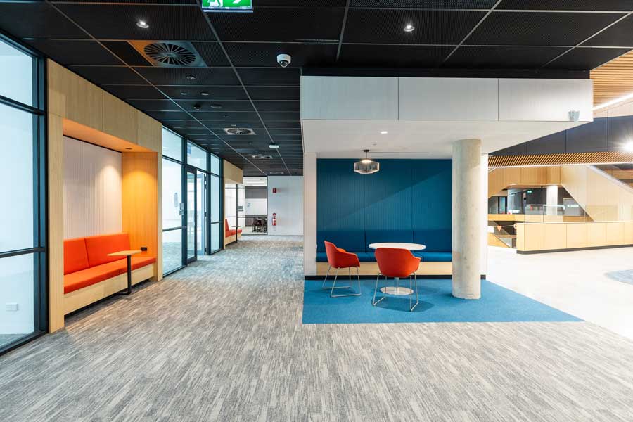 Modern indoor area with bright blue and orange furniture, featuring a student desks, seating areas, and large windows.